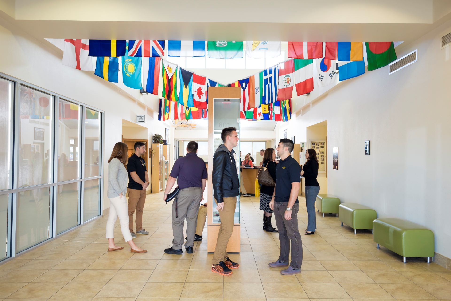 Students standing and talking in a hallway with international flags hanging from the ceiling